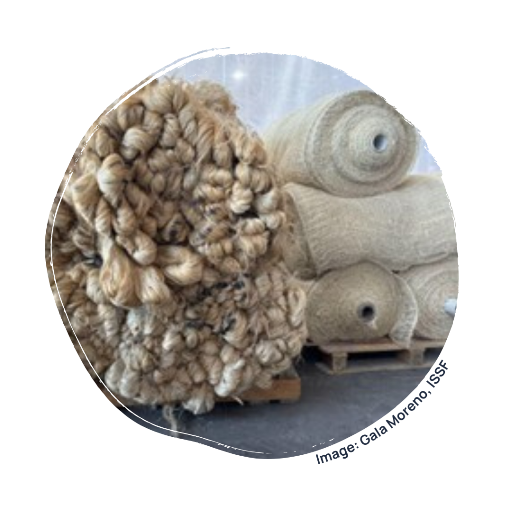 A large pile of spun and bundled material sits next to stacked rolls of woven material. Both are cream to brown in colour.